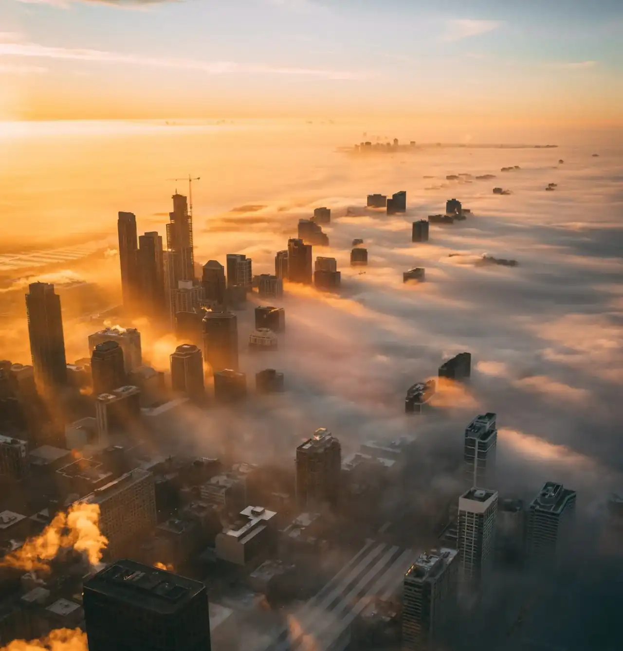Dubai towers rising through low cloud at sunrise, seen from above