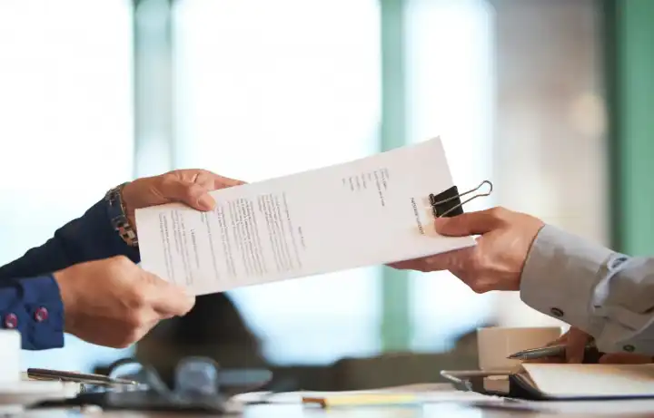 A clipped contract handed between two people across a desk